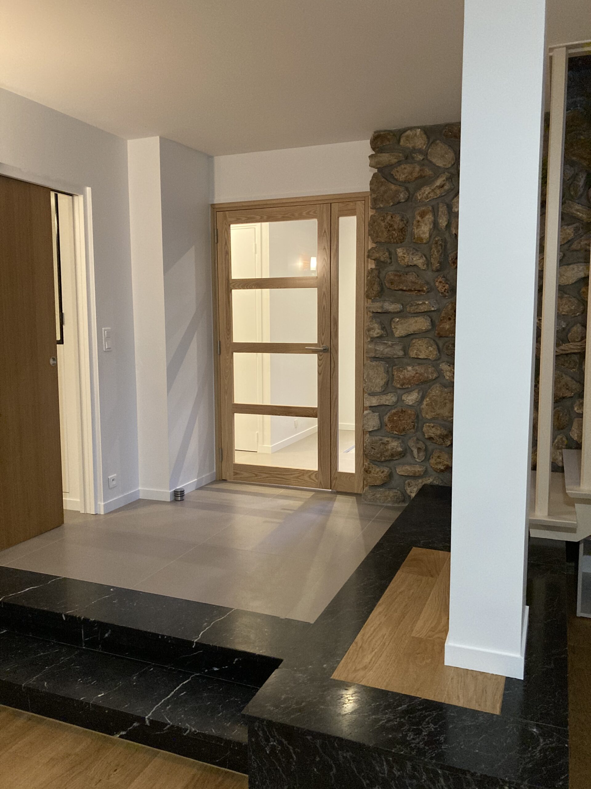 Rénovation intérieure et extérieure 45 77 91 94 - projet MG BATIMENT. Entrée rénovée avec porte vitrée en bois clair et mur en pierres naturelles.