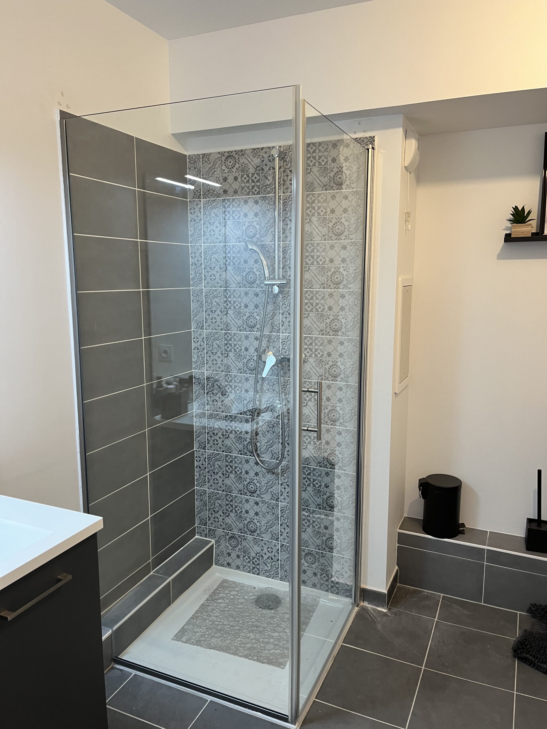 Rénovation intérieure et extérieure 45 77 91 94 - projet MG BATIMENT. Rénovation de salle de bain avec douche à l’italienne en angle, faïence grise et motifs géométriques.