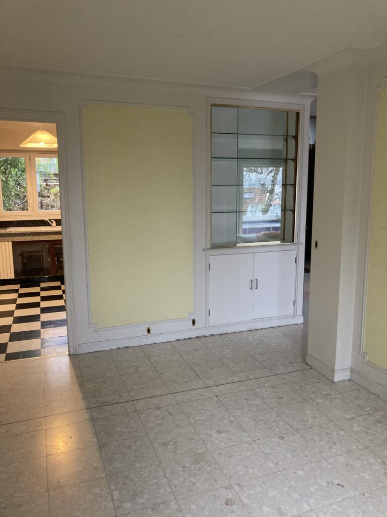 Vue d’un séjour avant rénovation avec sol en marbre clair et ouverture vers une cuisine