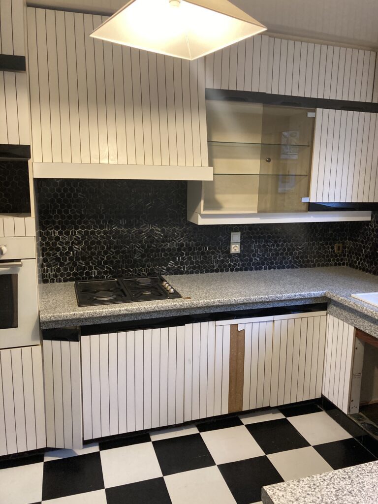Ancienne cuisine avec meubles à rayures verticales et carrelage noir et blanc