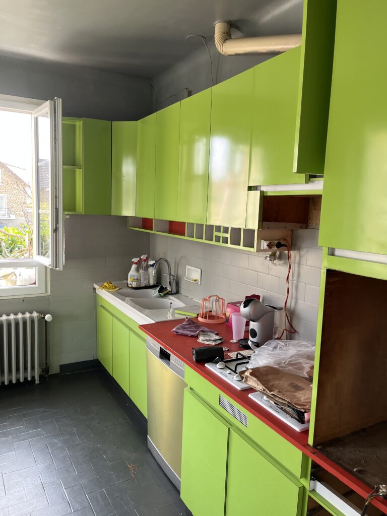 Cuisine ancienne avec meubles verts, sol noir et fenêtre