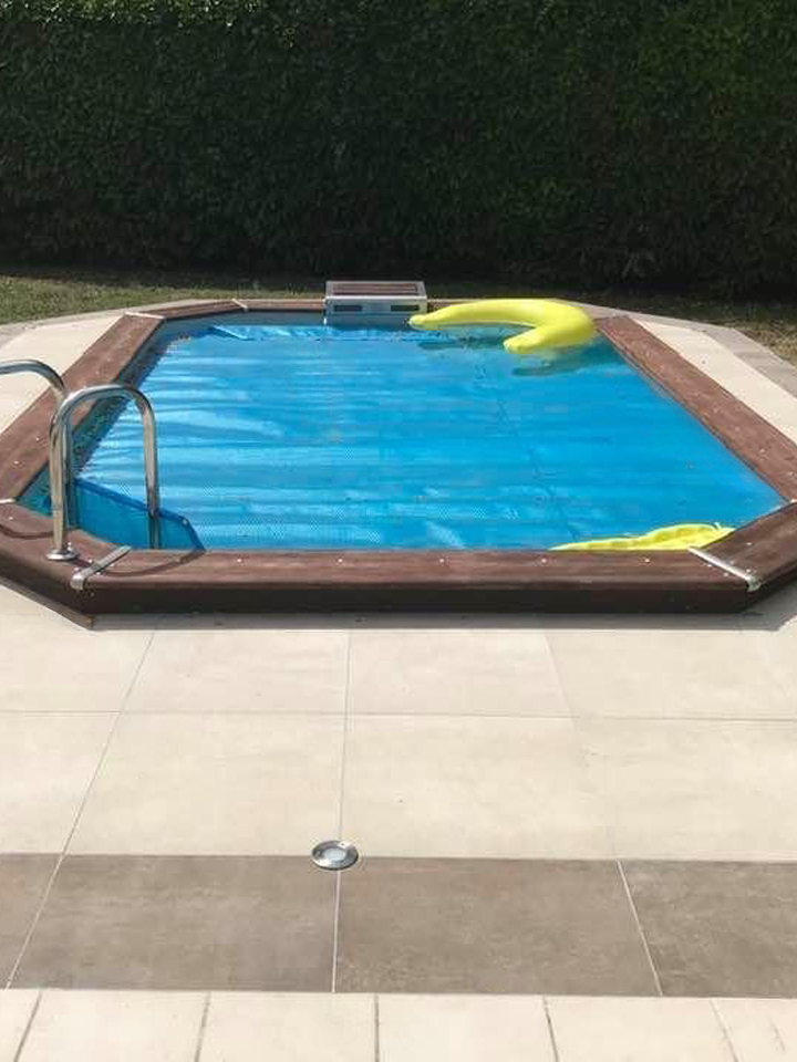 Piscine rénovée avec couverture bleue et plage en carrelage beige