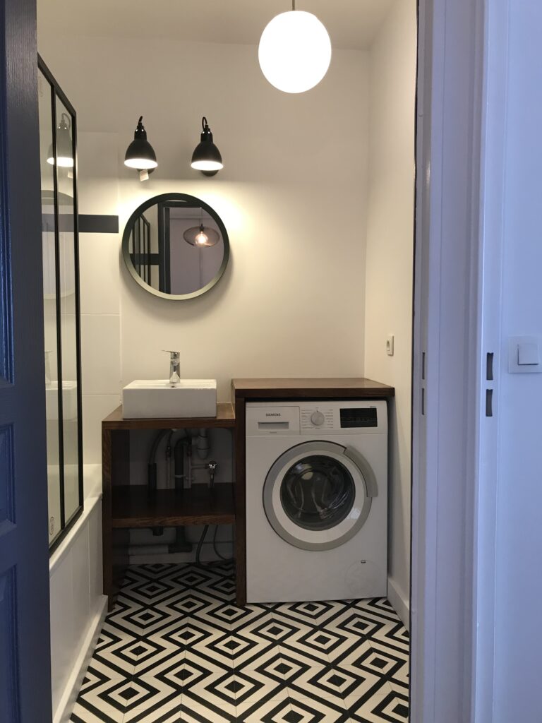 Salle de bain rénovée avec meuble bois, miroir rond et sol graphique