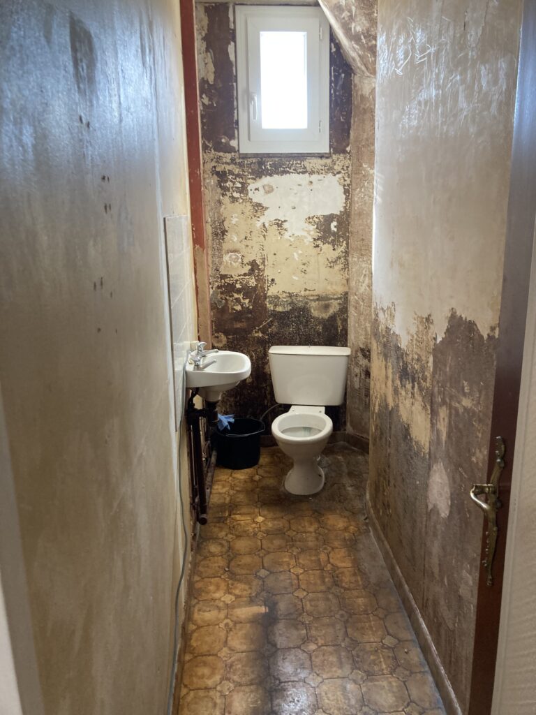 Vue des WC avant rénovation, murs abîmés et carrelage ancien